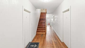 A narrow hallway with wooden flooring, white walls, and a wooden staircase leading to an upper level.