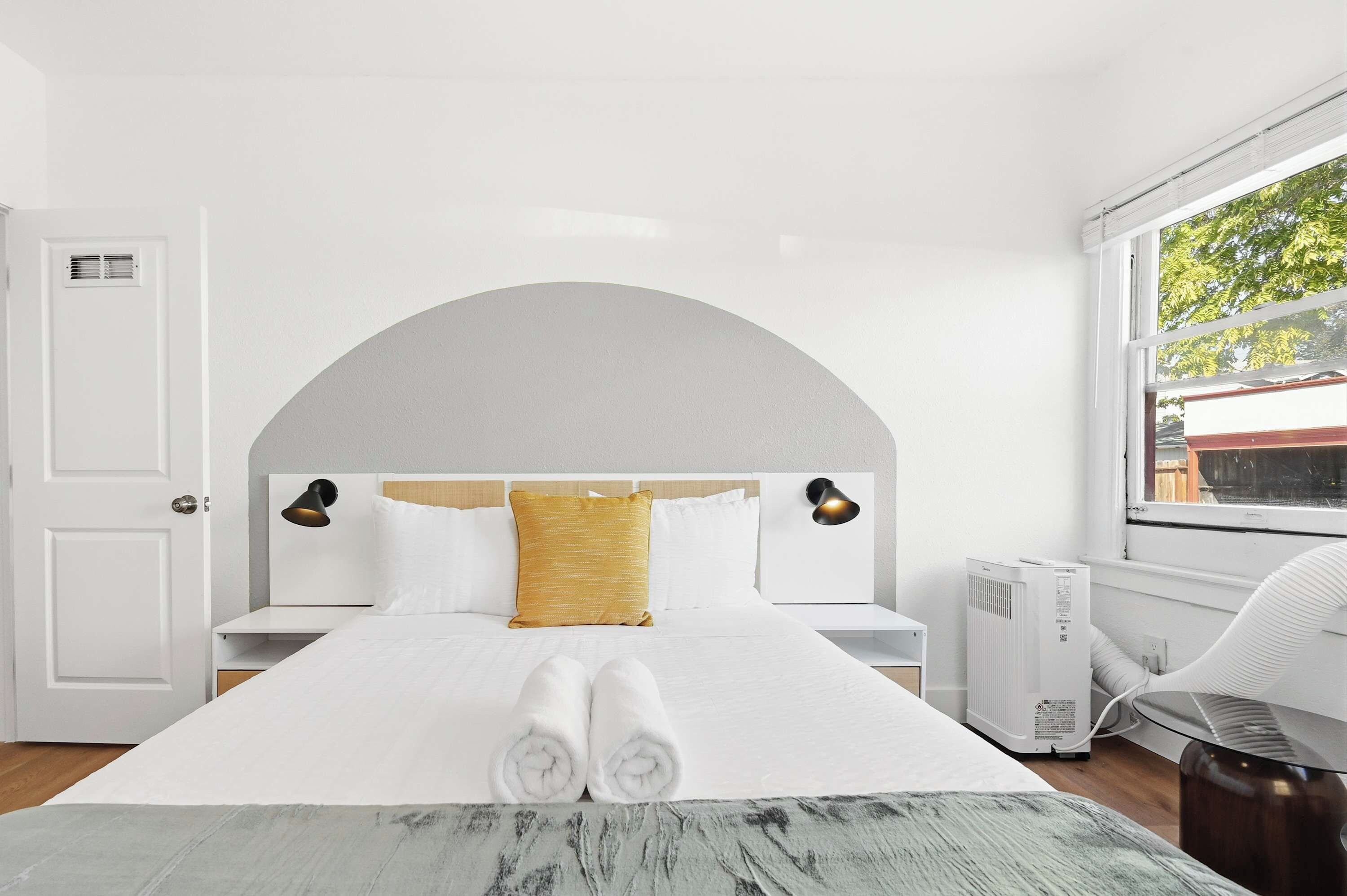 A modern bedroom with a large bed, two bedside tables, a window with a view, and a radiator.