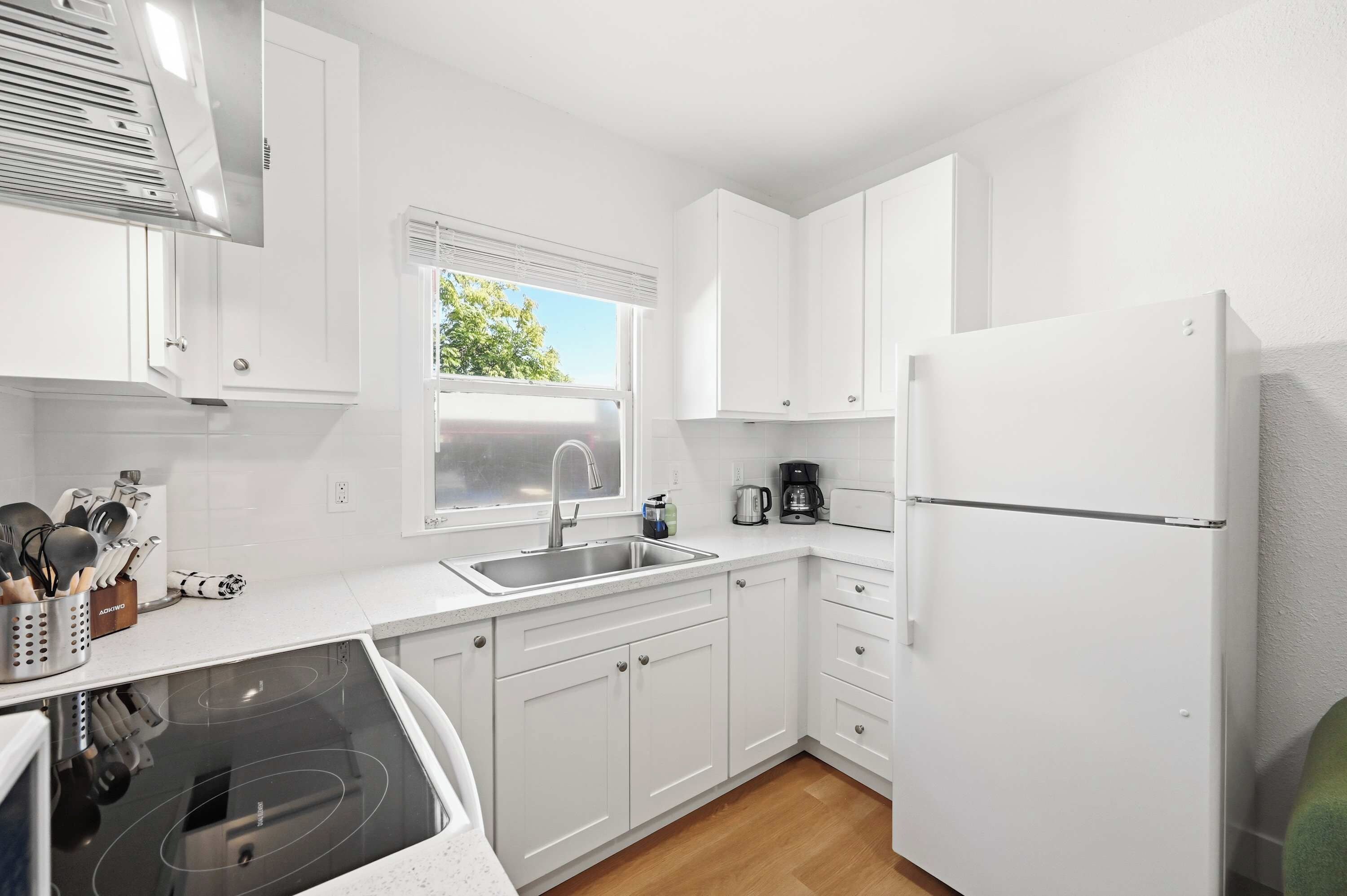 A modern kitchen with white cabinets, a stainless steel sink, a built-in oven, and a refrigerator.