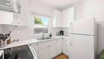 A modern kitchen with white cabinets, a stainless steel sink, a built-in oven, and a refrigerator.
