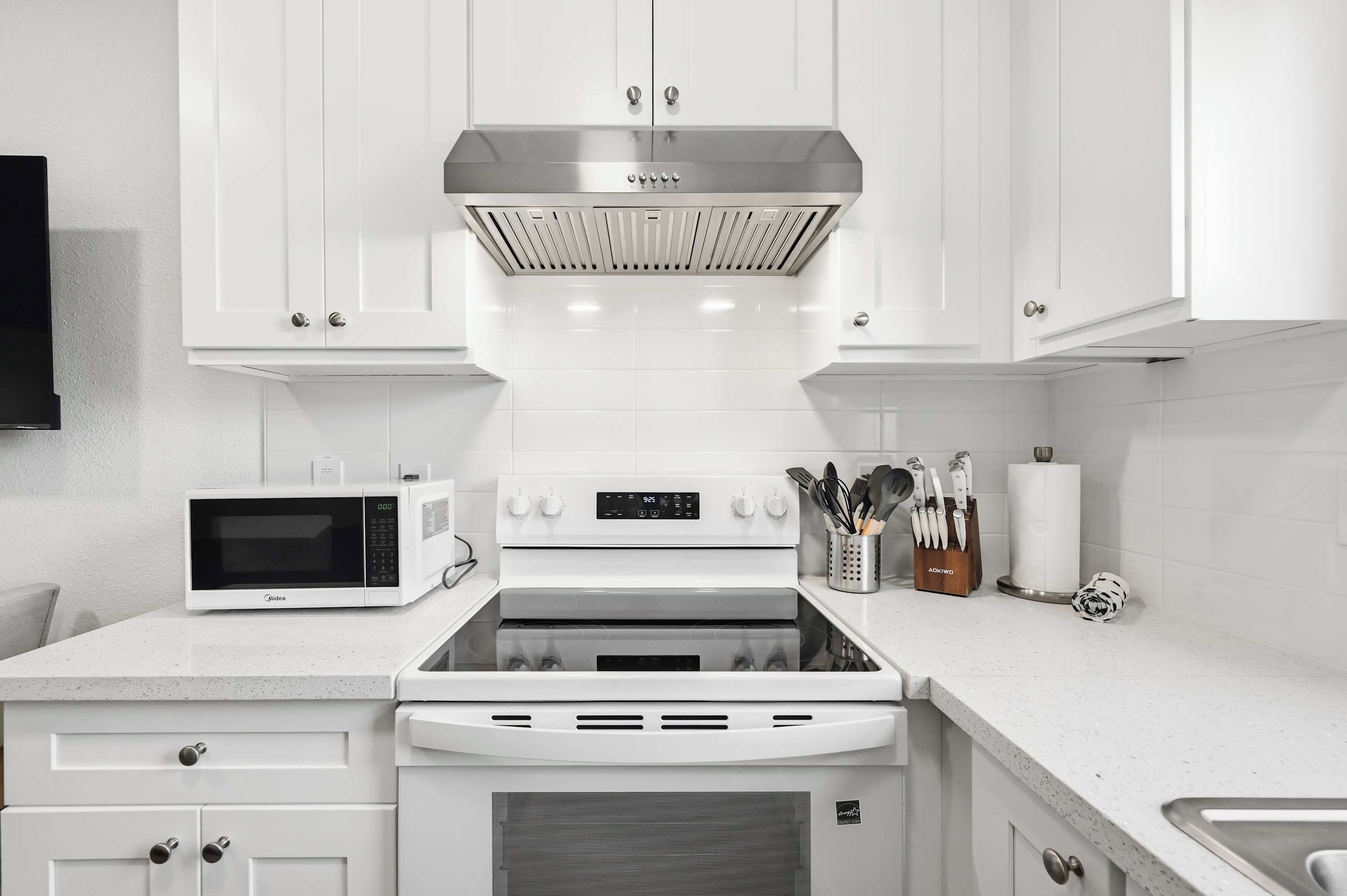A modern kitchen with white cabinetry, a stainless steel range hood, a microwave, and an oven.