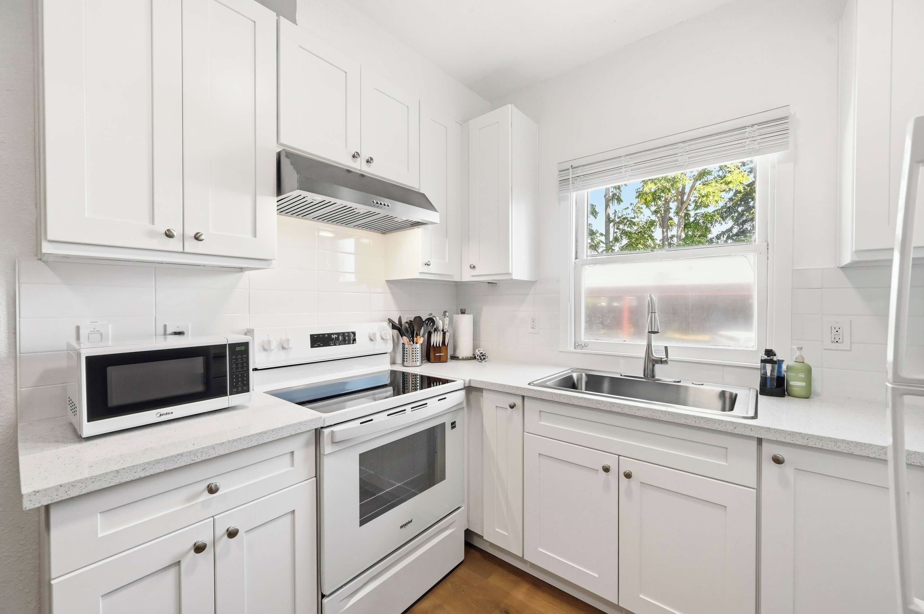 A modern kitchen with white cabinetry, a built-in microwave, oven, and a window with a view of trees.