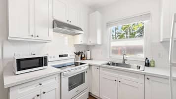 A modern kitchen with white cabinetry, a built-in microwave, oven, and a window with a view of trees.