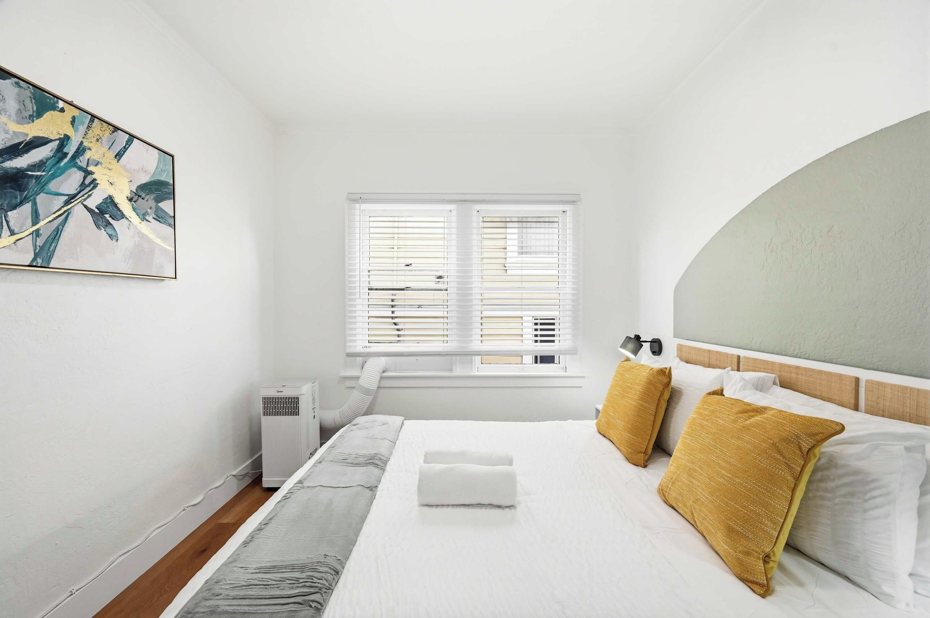 A bedroom with a bed, a window with blinds, a radiator, and a painting on the wall.