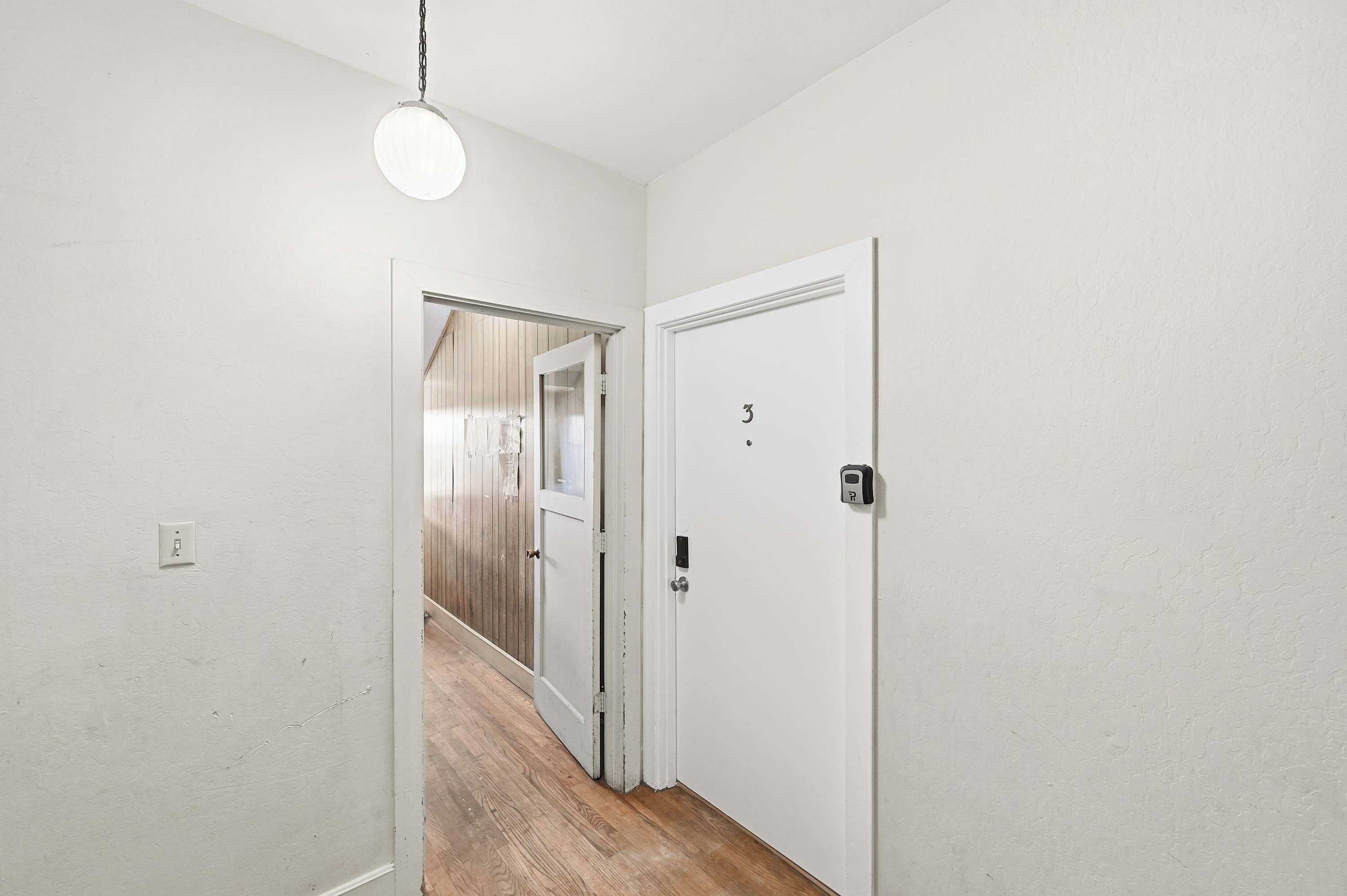 A hallway with a white door, a light fixture, and a wooden floor.