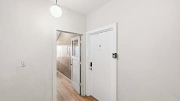 A hallway with a white door, a light fixture, and a wooden floor.