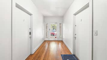 A hallway with white walls and wooden flooring leading to a door with a glass panel.