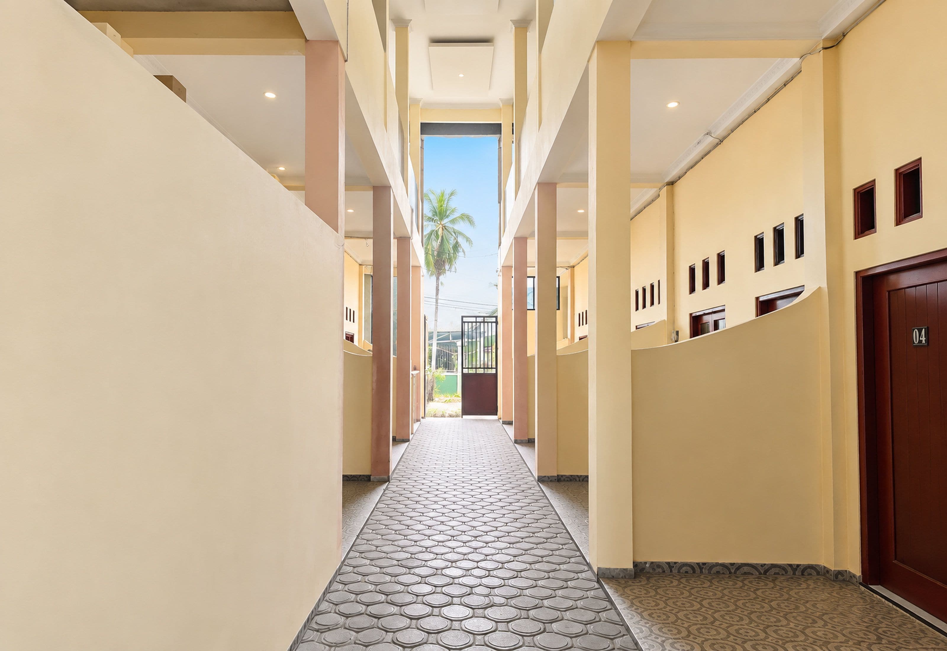 A hotel corridor with a tiled floor, a palm tree outside, and a door marked with the number 04.