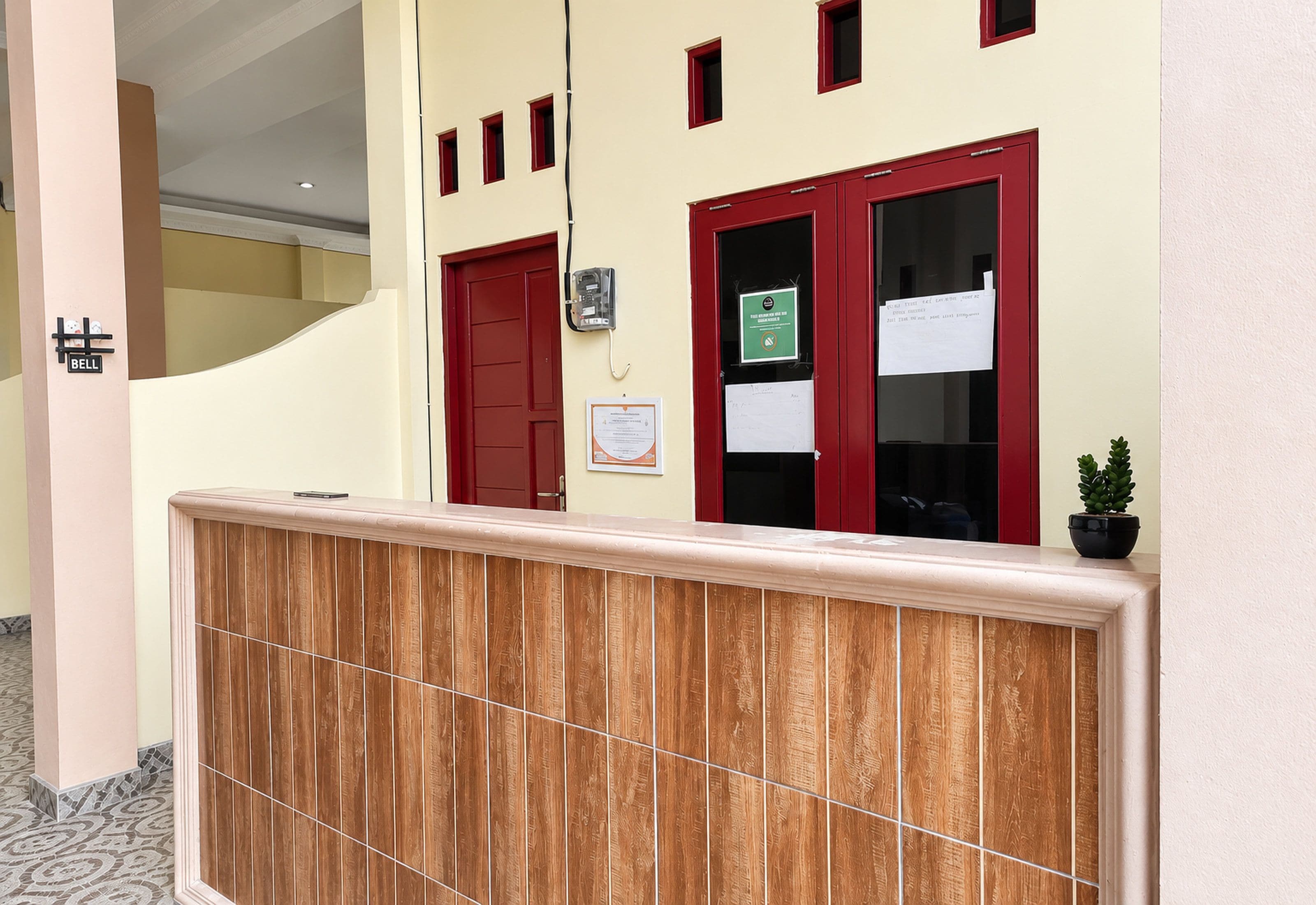 A reception area with a wooden reception desk, red doors, and a small potted plant.