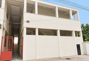 Um edifício de dois andares com escadaria central, janelas amplas e um portão vermelho.