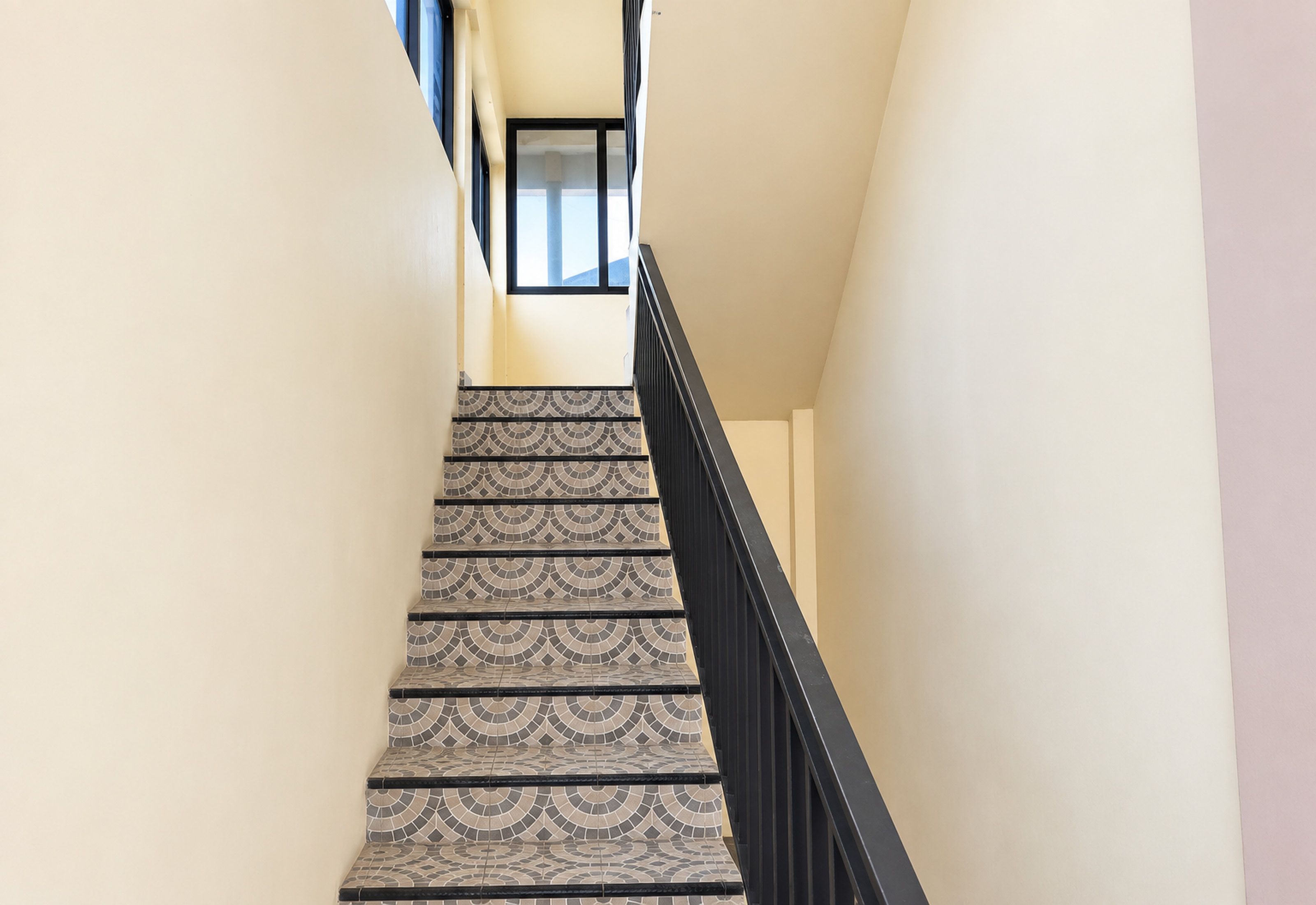 A staircase with patterned tiles and a black railing, leading to a landing with a window.