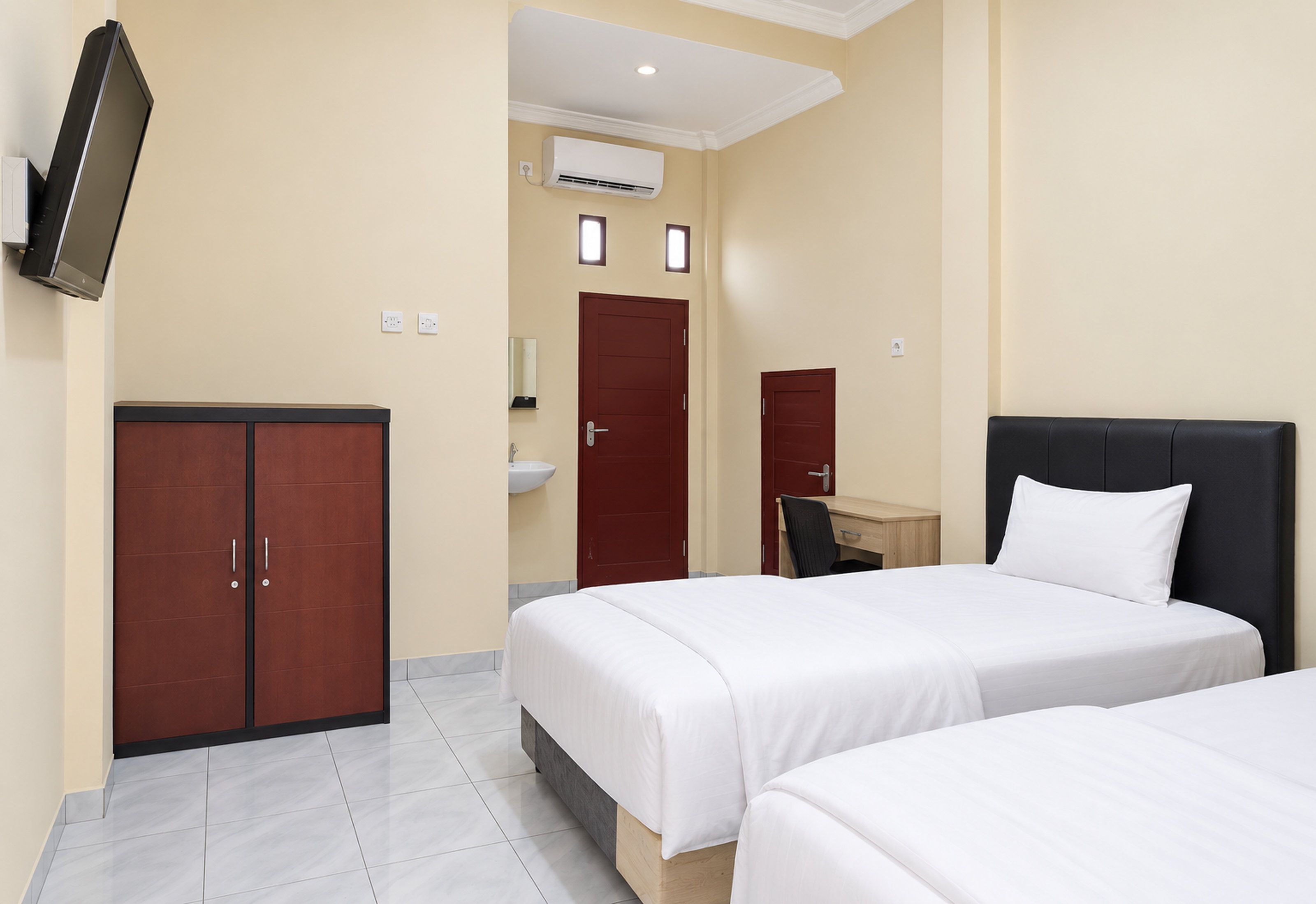 Quarto de hotel com duas camas, uma escrivaninha, um guarda-roupa, um espelho e um aparelho de ar condicionado.