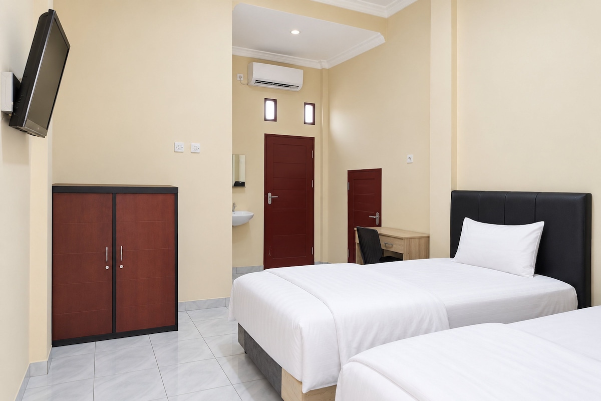 Quarto de hotel com duas camas, uma escrivaninha, um guarda-roupa, um espelho e um aparelho de ar condicionado.