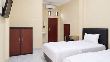 Quarto de hotel com duas camas, uma escrivaninha, um guarda-roupa, um espelho e um aparelho de ar condicionado.
