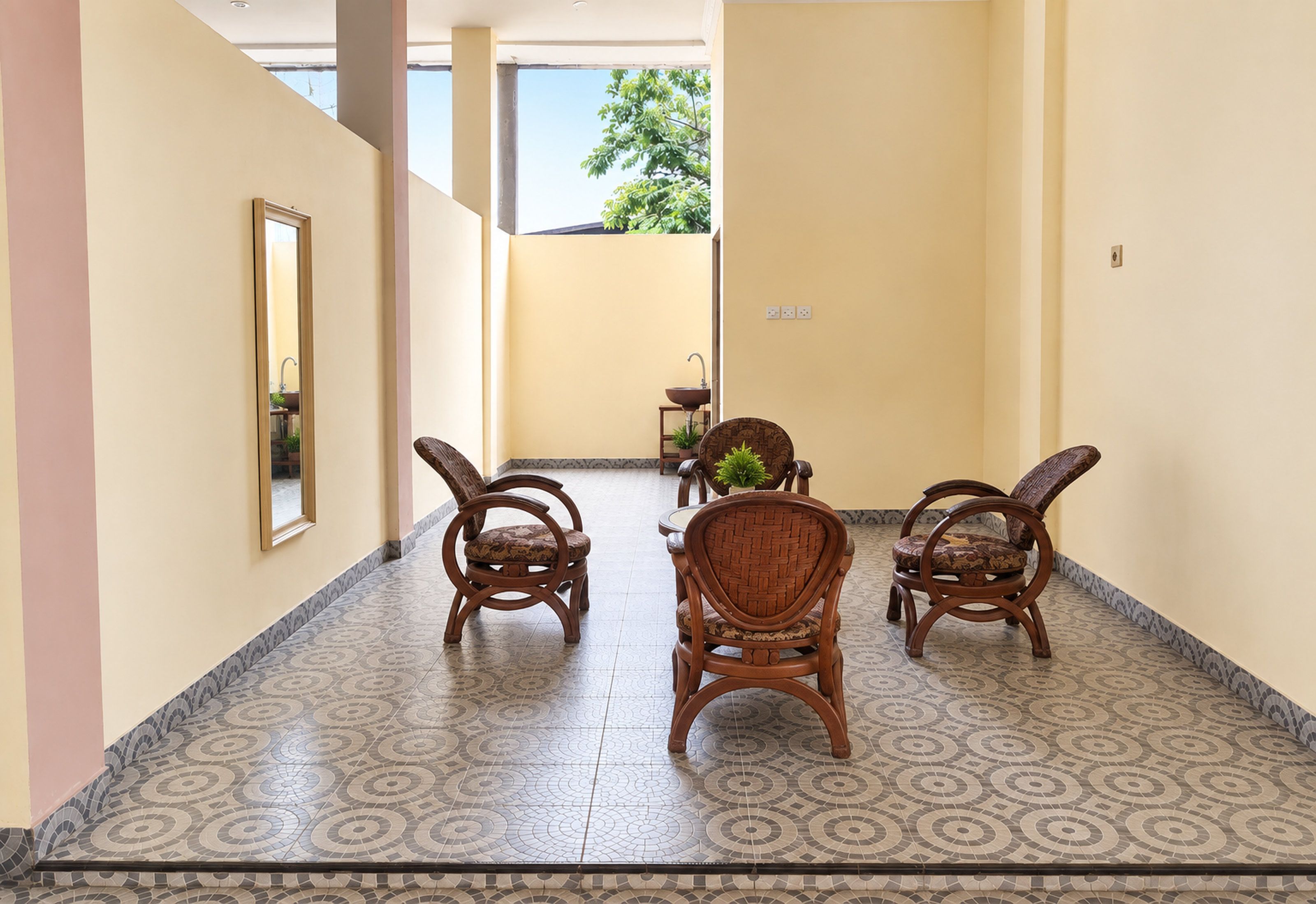 A hallway with patterned floor tiles, a mirror, and two wooden chairs with cushions.