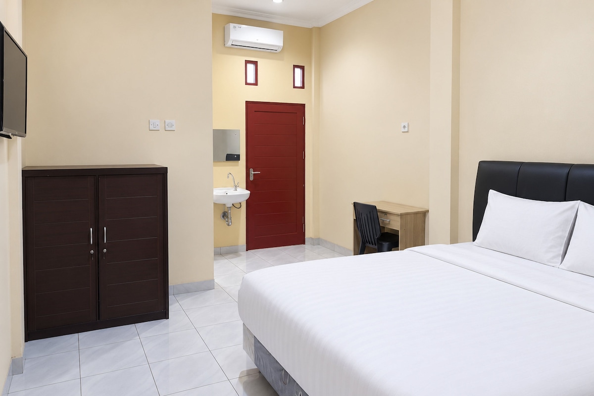 Quarto de hotel com cama, guarda-roupa, escrivaninha e cadeira, pia e ar condicionado.