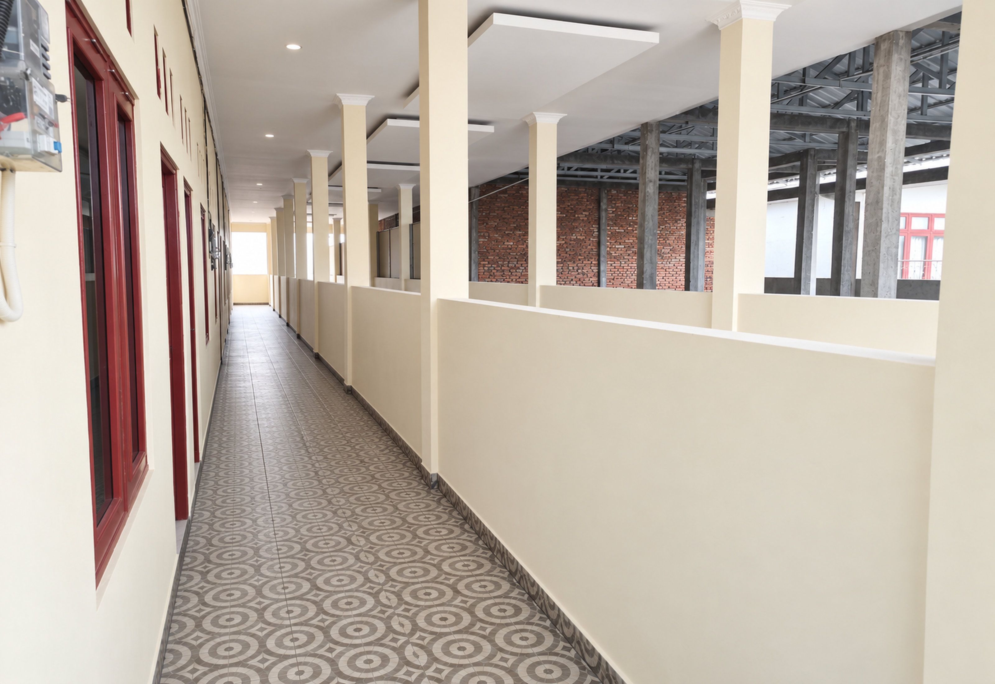 Un couloir doté d’un sol à motifs, de murs blancs et de fenêtres aux encadrements rouges.