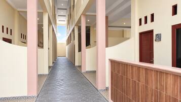 Um corredor com chão de azulejos, colunas e um corrimão de madeira à direita.