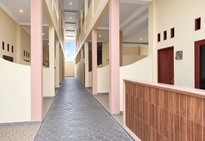 Um corredor com chão de azulejos, colunas e um corrimão de madeira à direita.