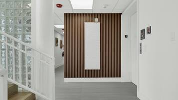 A modern interior with a wooden panel wall, a staircase with glass railings, and a hallway with a tiled floor.