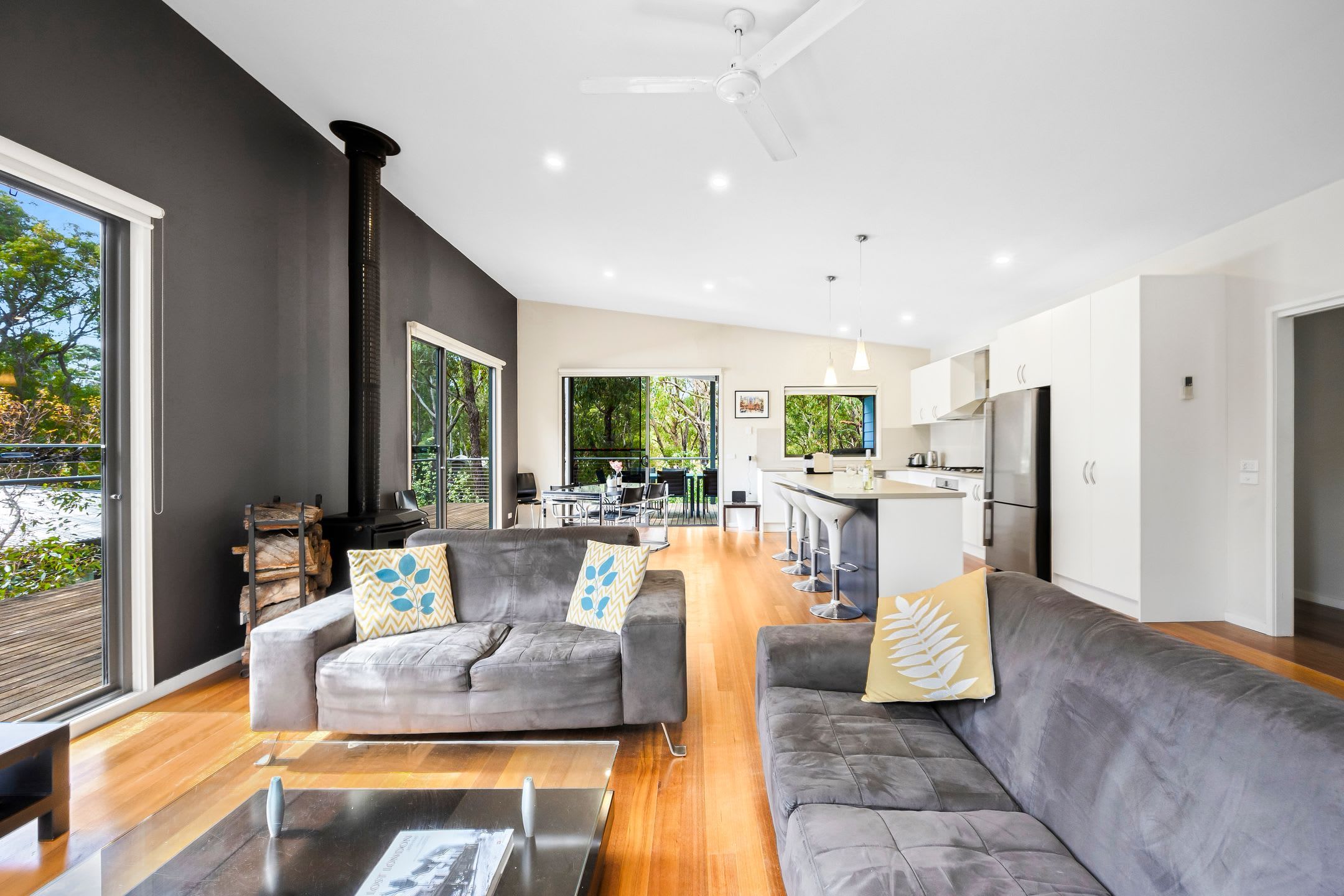 A modern living room with a fireplace, grey sofas, and a dining area with a kitchen in the background.