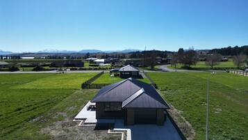 Une propriété rurale comprenant un bâtiment principal et une dépendance plus petite, le tout entouré de champs ouverts et surplombant des montagnes lointaines.