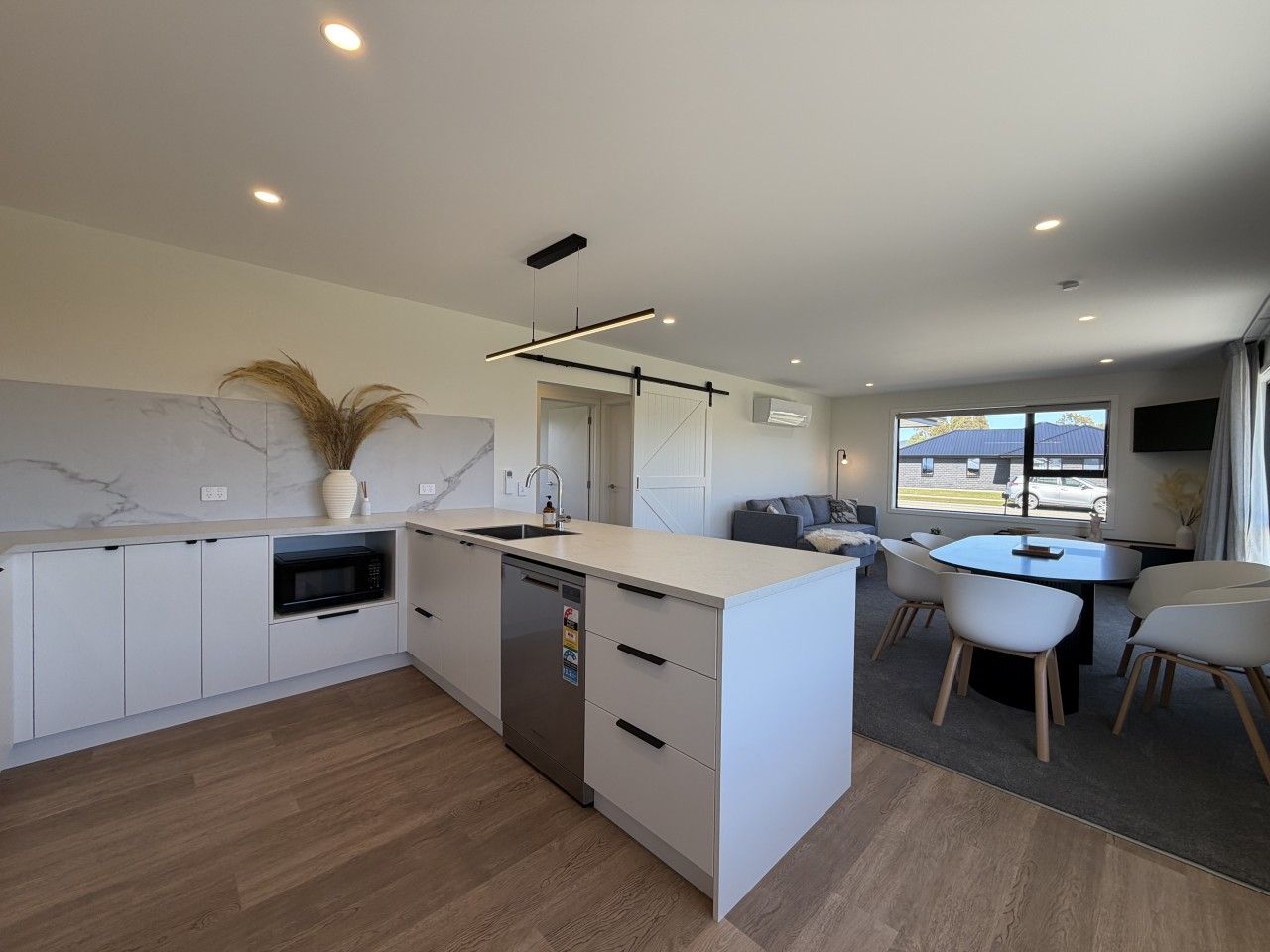 Een moderne keuken met een centraal eiland, inbouwapparatuur en een eethoek met een ronde tafel en stoelen.