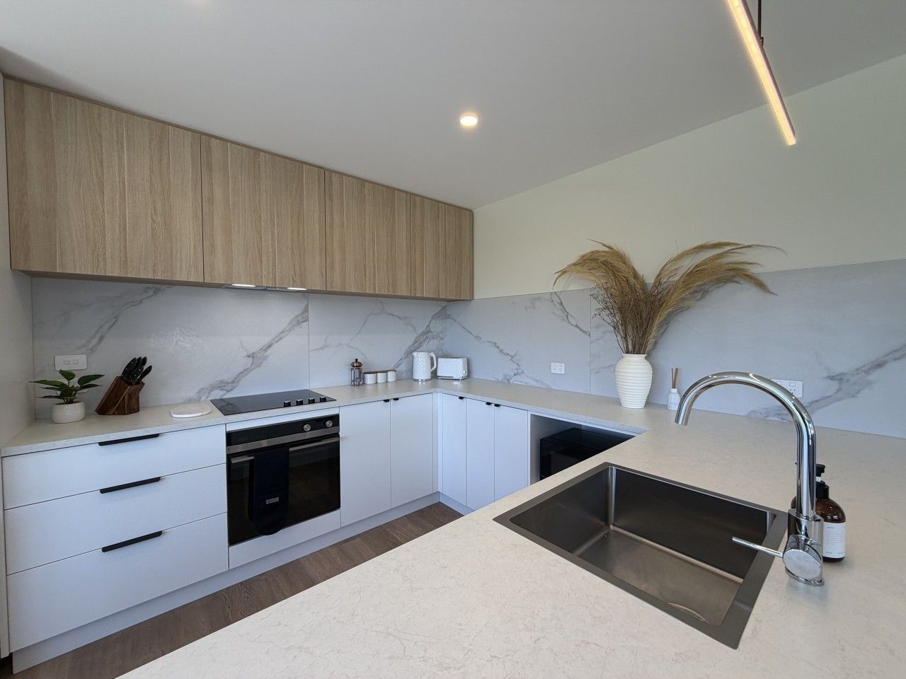 A modern kitchen with white cabinetry, a built-in oven, and a stainless steel sink.