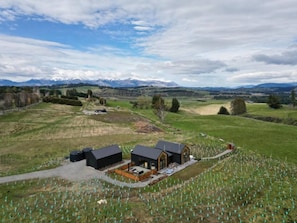 A rural property with a farmhouse, a fenced garden, and a view of distant mountains. - Kākāpō Nest | Sauna, Outdoor Bath, Mountain Views (Te Anau)