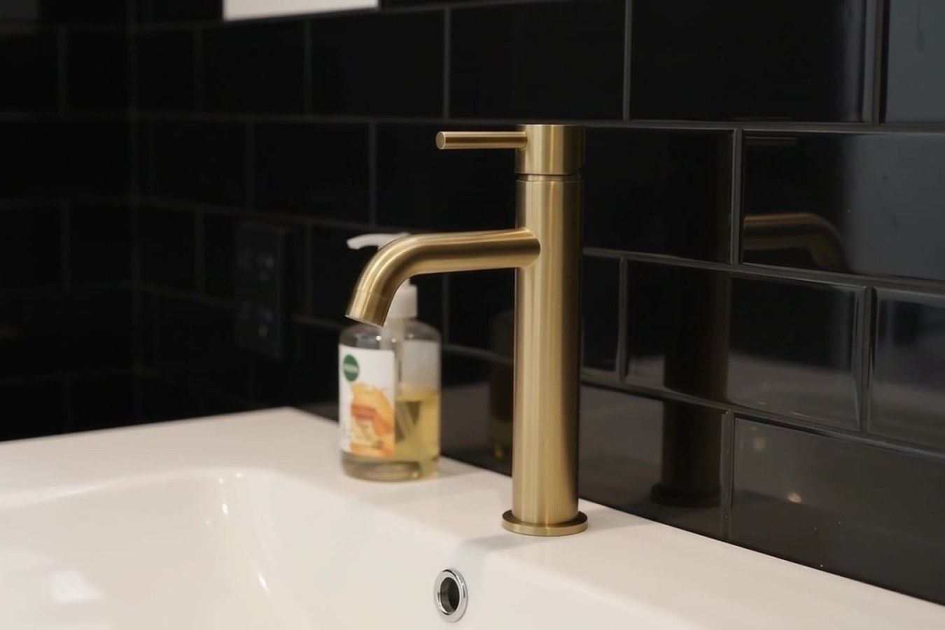 A bathroom sink with a gold faucet and a soap dispenser.