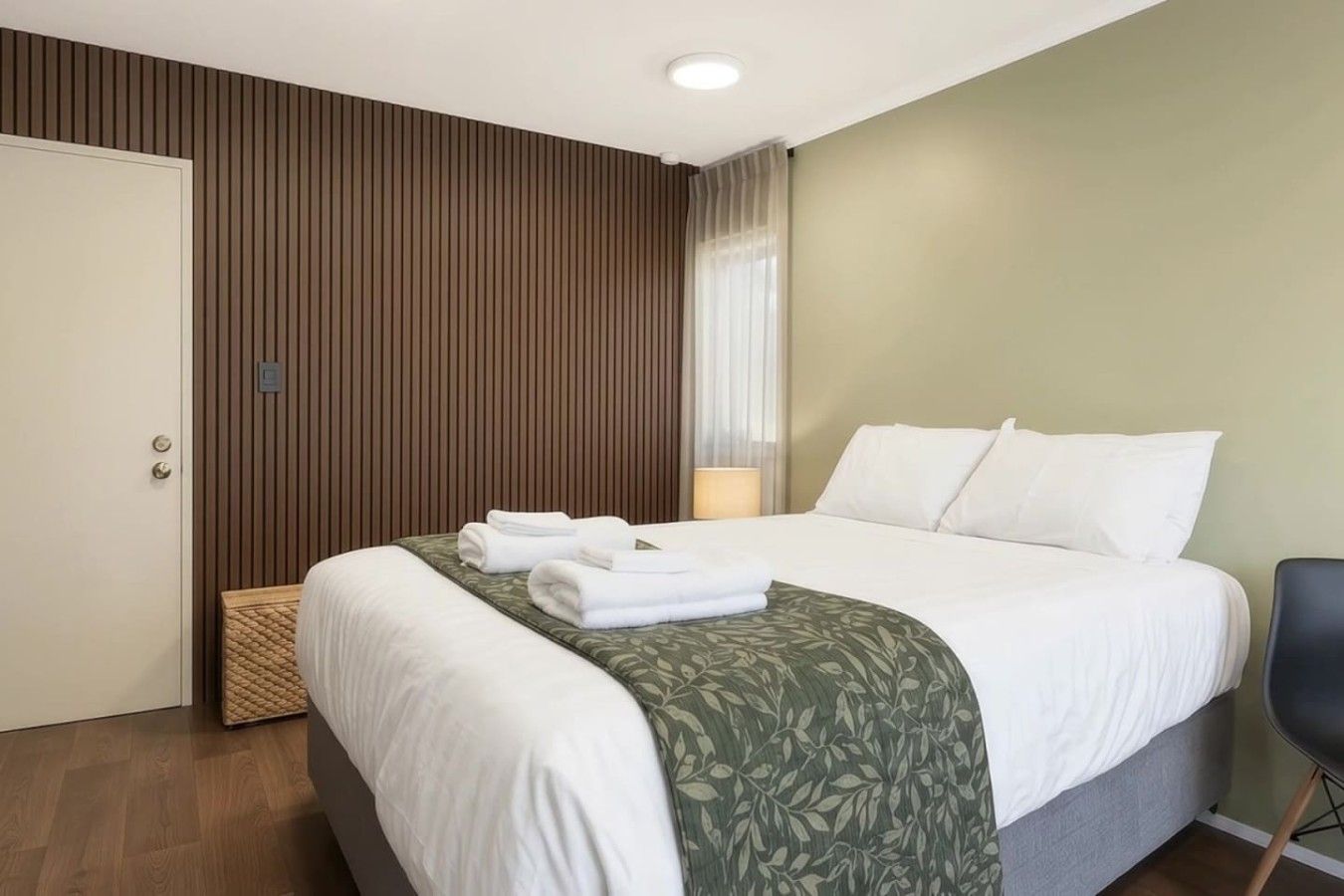 A hotel room with a bed, a bedside table, a lamp, and a door.