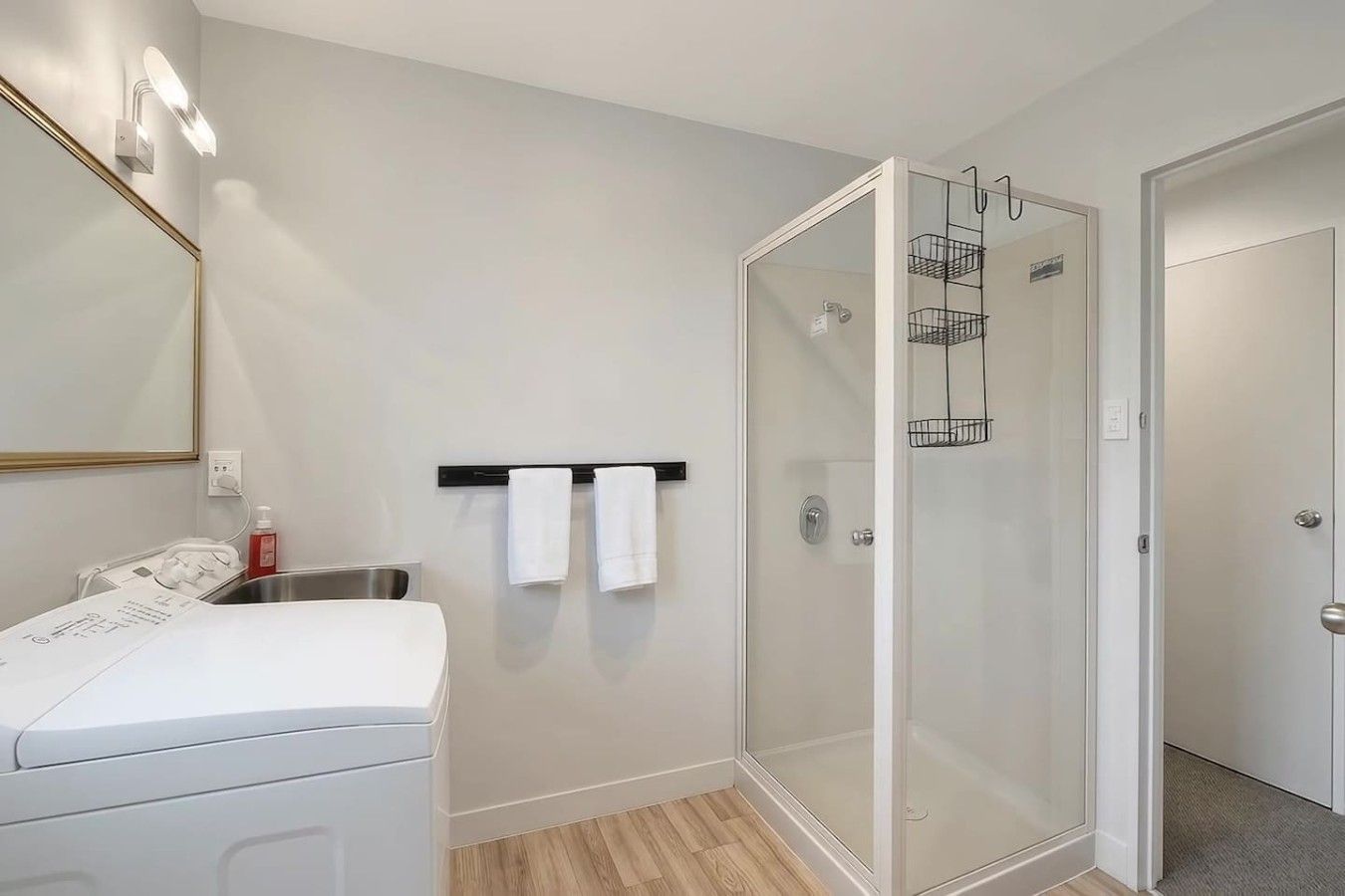 Ein modernes Badezimmer mit Duschkabine aus Glas, einer weißen Waschmaschine und einem Handtuchhalter mit zwei Handtüchern.