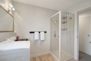 Une salle de bain moderne avec une douche à parois de verre, un lave-linge blanc et un porte-serviettes avec deux serviettes.
