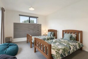 A bedroom with two wooden beds, a window, a radiator, a bedside table, and a bean bag chair. - Beyond the Bay | Rural Riverton Escape (Riverton/Aparima)
