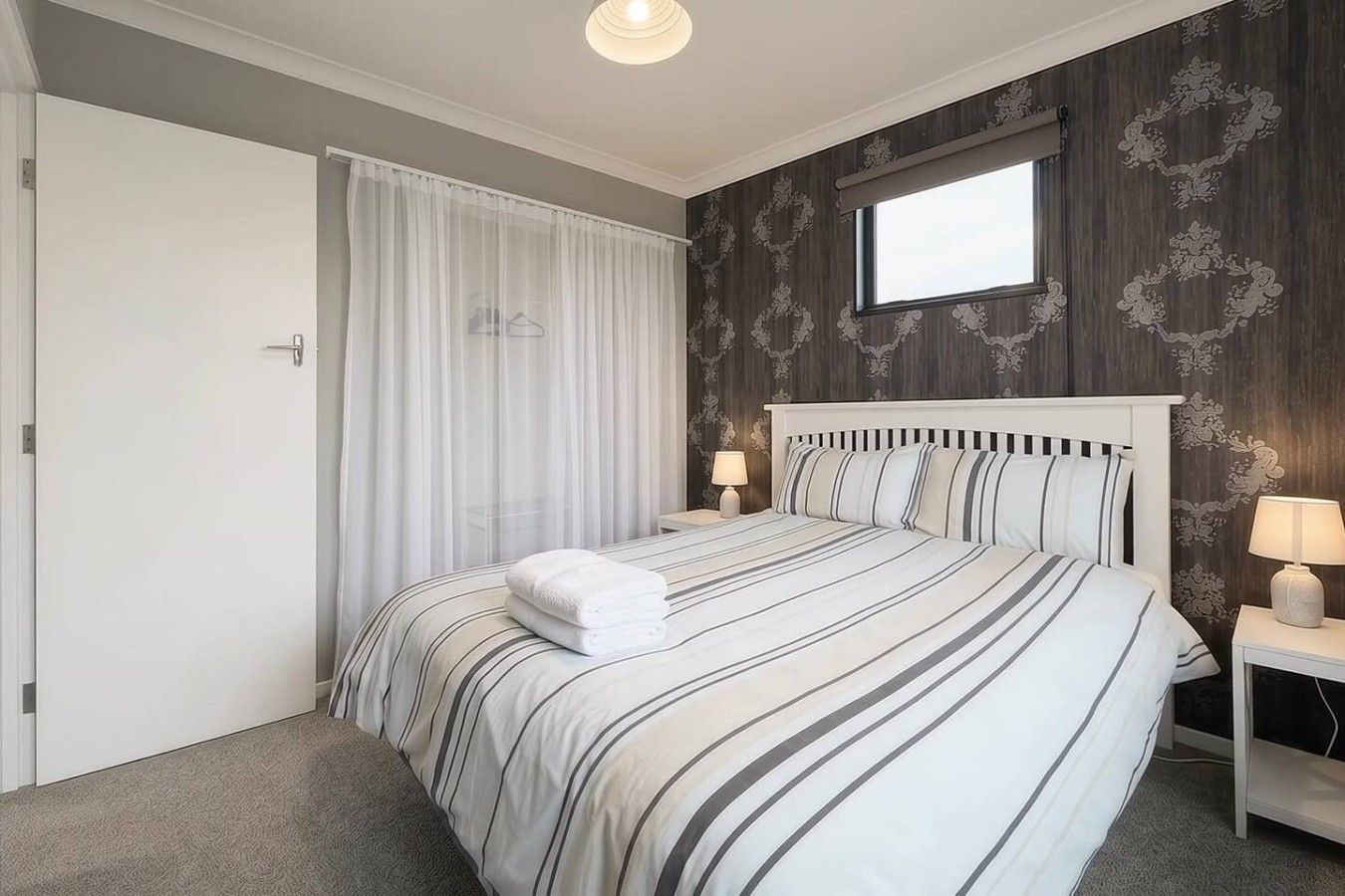 Et hotelværelse med en seng, to sengeborde, et vindue og en dør.