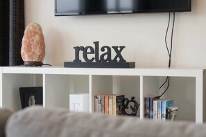 A white entertainment center with a 'relax' sign, a salt lamp, and books. - Beyond the Bay | Rural Riverton Escape (Riverton/Aparima)