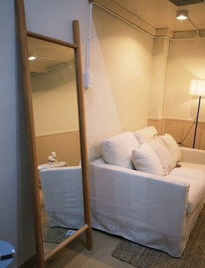 Une chambre d’hôtel avec un lit, un miroir, une lampe et une petite table sur laquelle se trouve une bouteille.
