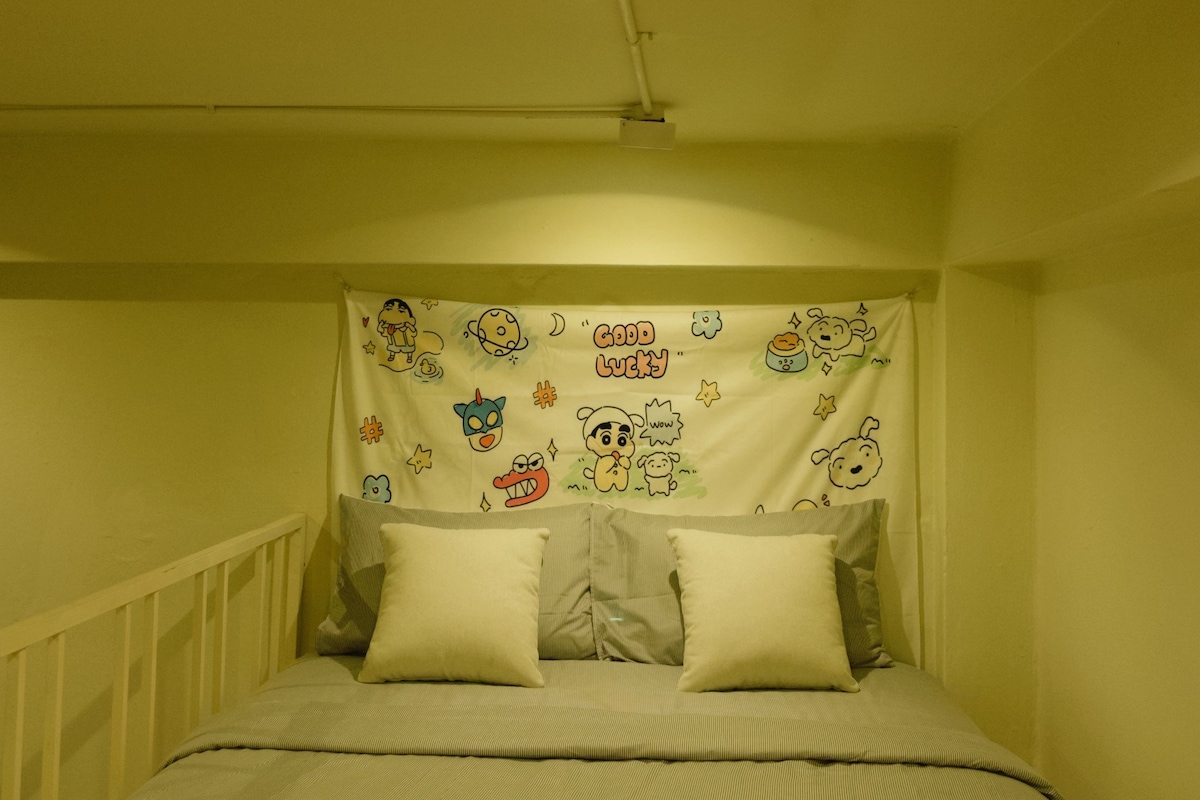 Une chambre à coucher avec un lit, des oreillers, une tête de lit ornée d’un motif de dessin animé et un luminaire au plafond.