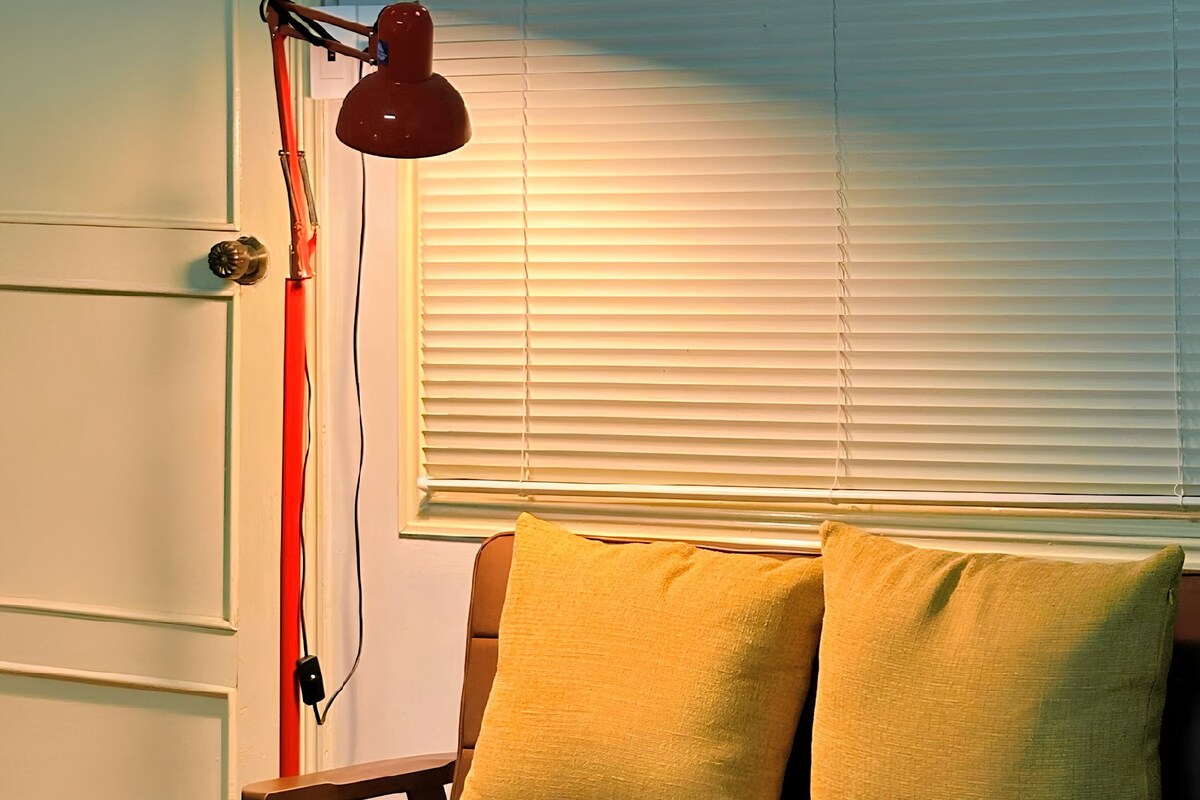Una habitación con un sofá de cuero marrón, una mesa de centro de vidrio y una lámpara de pie roja.