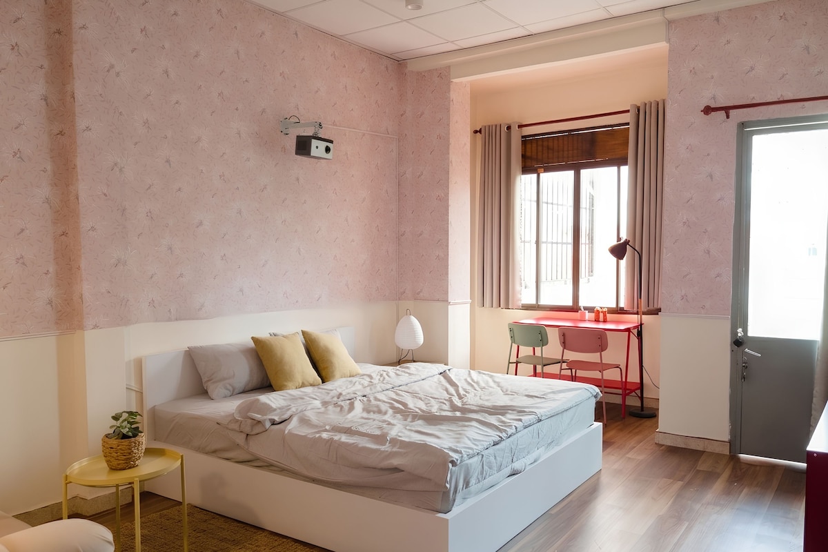 Un dormitorio con cama, una mesita, una silla, un escritorio y una ventana con cortinas.