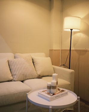 Une pièce chaleureuse avec un canapé, une table ronde sur laquelle repose un livre et un lampadaire.