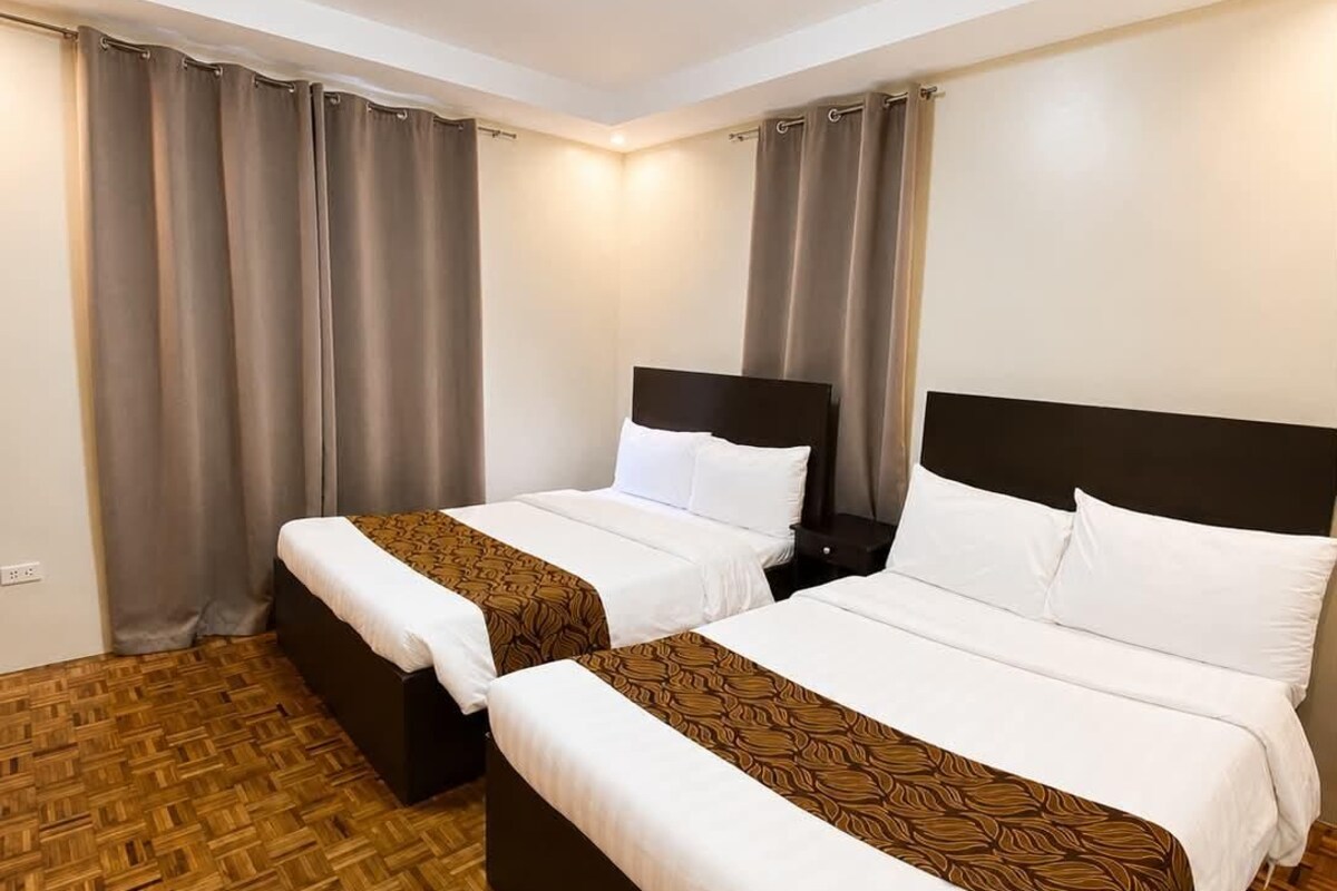 Habitación de hotel con dos camas, piso de parqué de madera y una lámpara en el techo.
