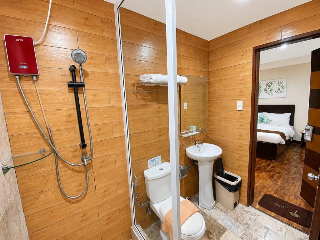A bathroom with a wooden wall, a glass shower enclosure, a toilet, a sink, and a red electric heater.