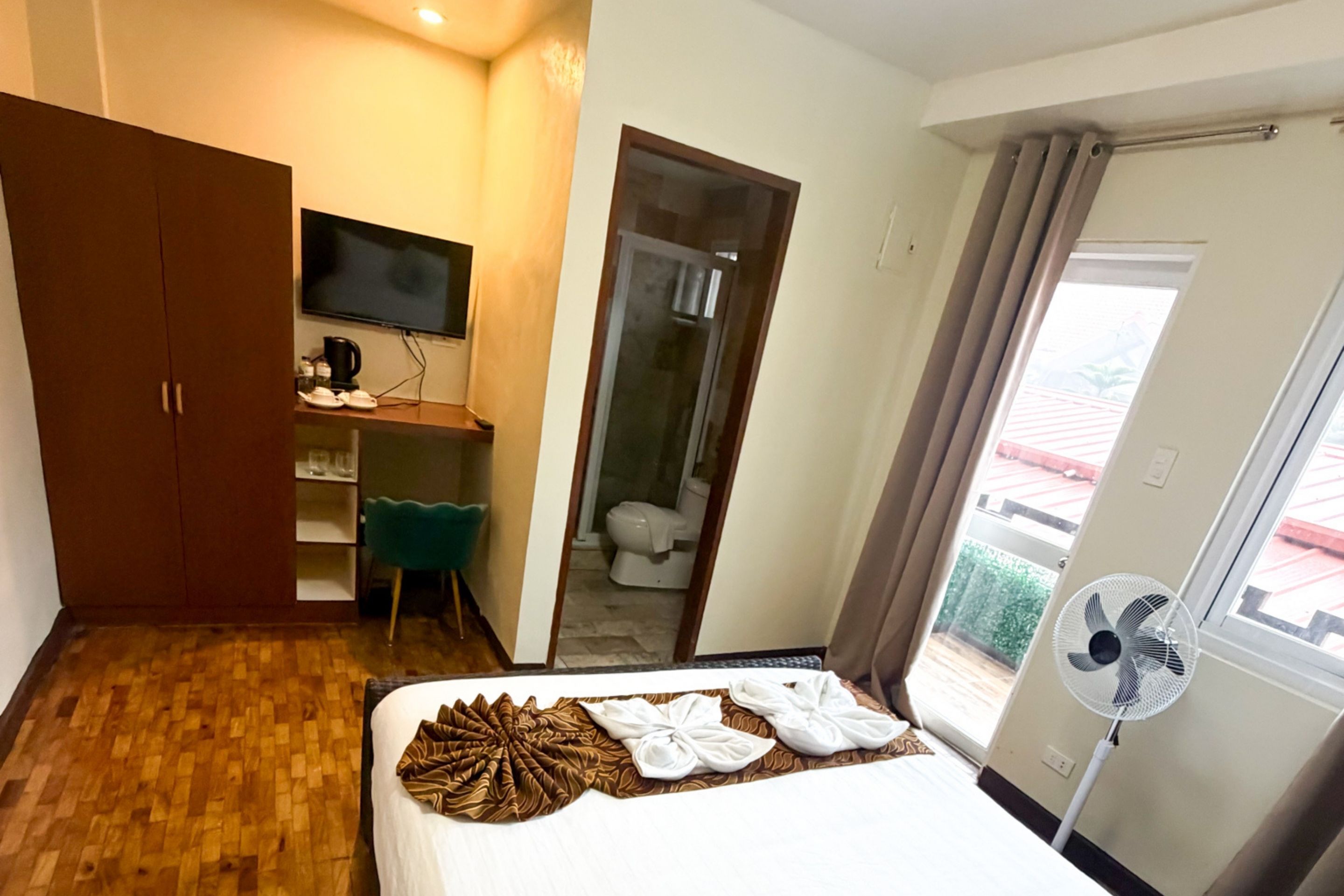 A hotel room with a bed, a television, a desk with a chair, a wardrobe, and a bathroom visible through an open door.