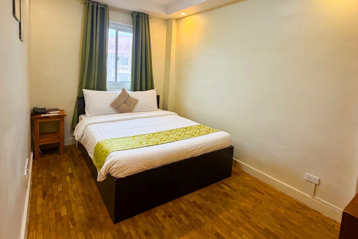 Una habitación de hotel con una cama individual, una mesita de noche y un ventanal con cortinas.