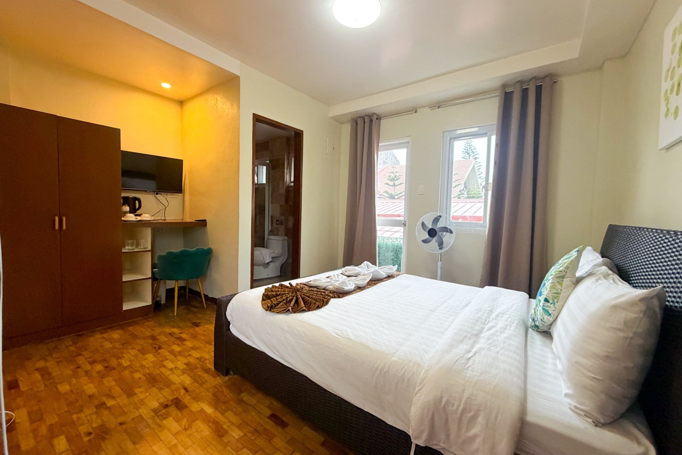 A hotel room with a bed, a desk, a chair, a wardrobe, and a bathroom visible through an open door.