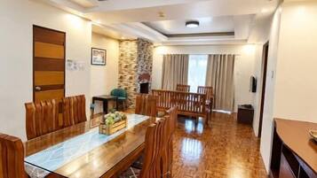 A spacious dining area with a wooden table and chairs, a stone accent wall, and a view into another room.