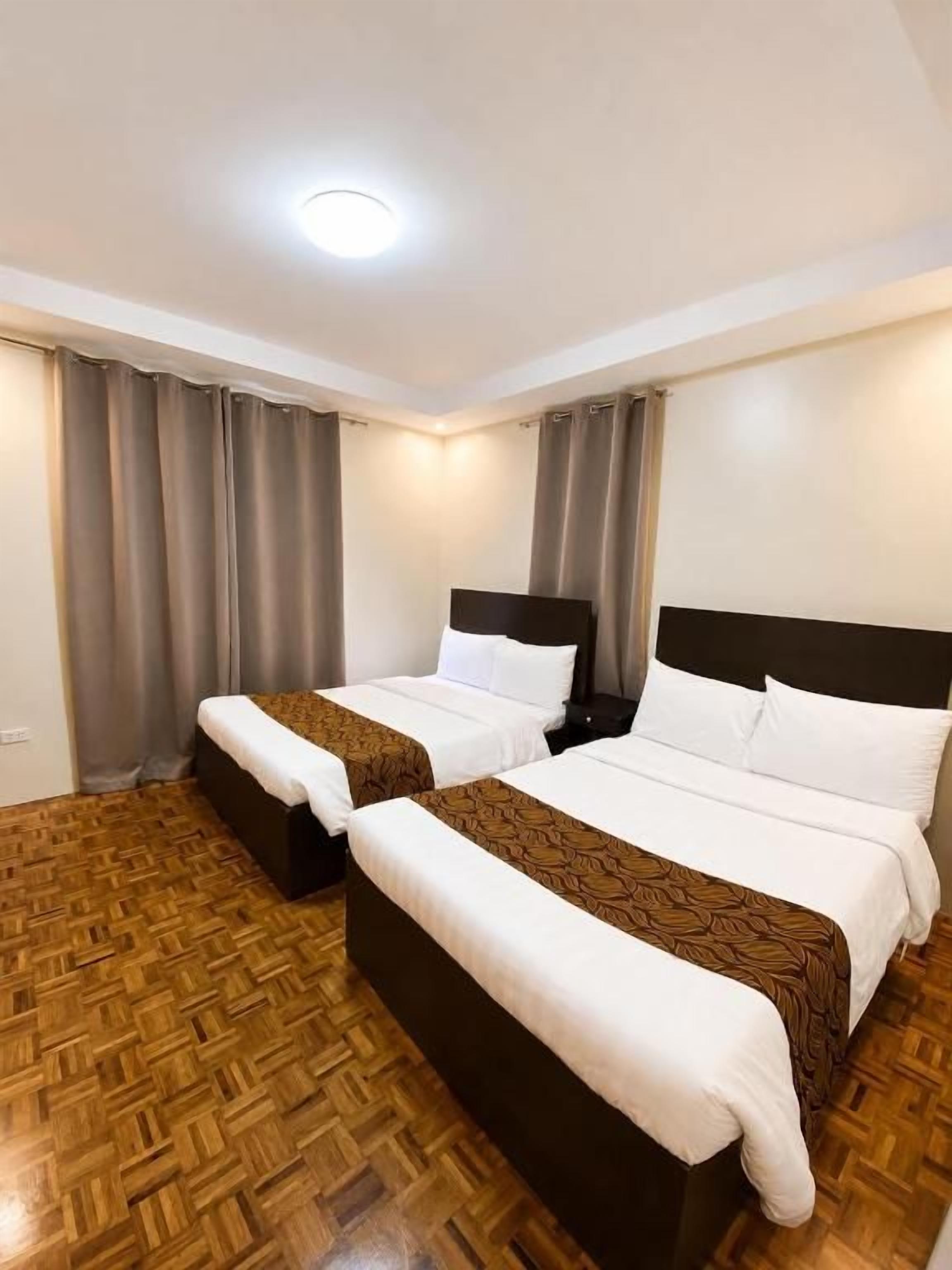 A hotel room with two beds, a wooden floor, and a ceiling light.