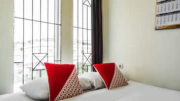 A hotel room with a bed, two pillows, a calendar on the wall, and a window with a view of buildings.
