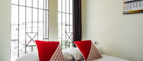 A hotel room with a bed, two pillows, a calendar on the wall, and a window with a view of buildings.
